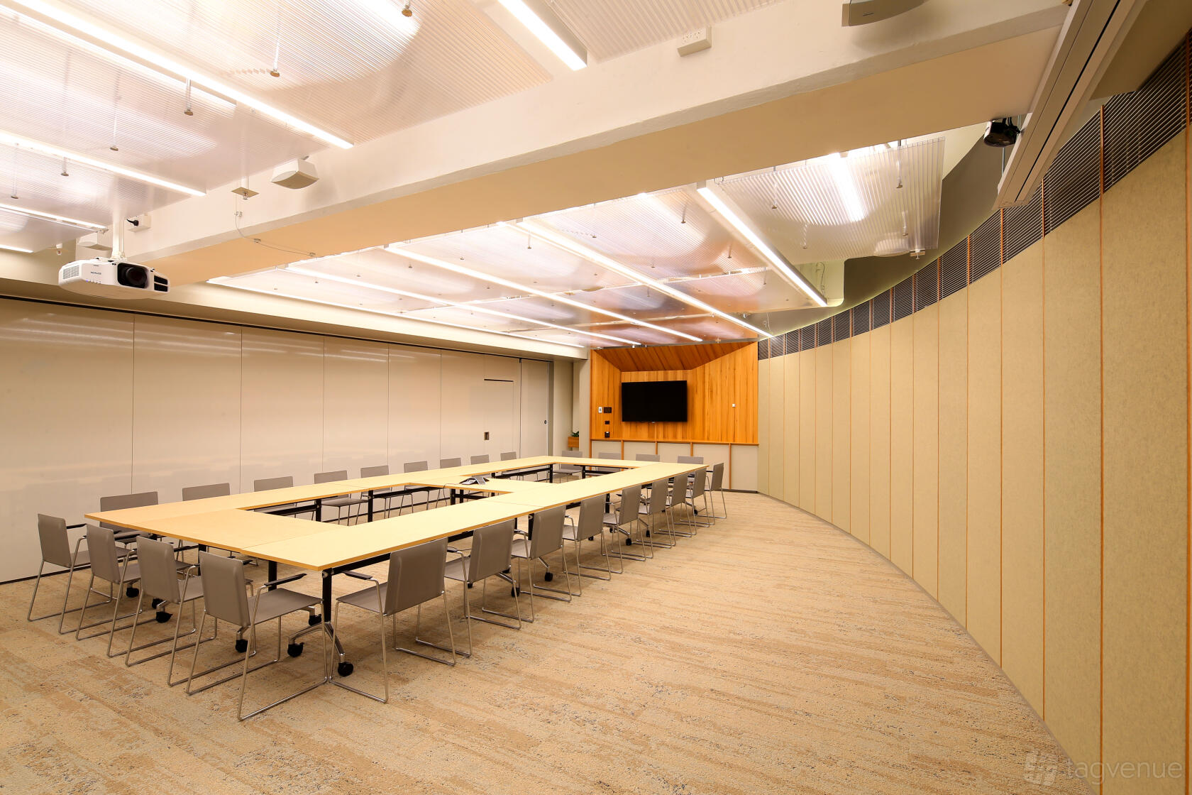 A meeting room with a U-shaped table arrangement, ceiling lights, and wall-mounted screens at Flex by ISPT at 477 on Pitt.