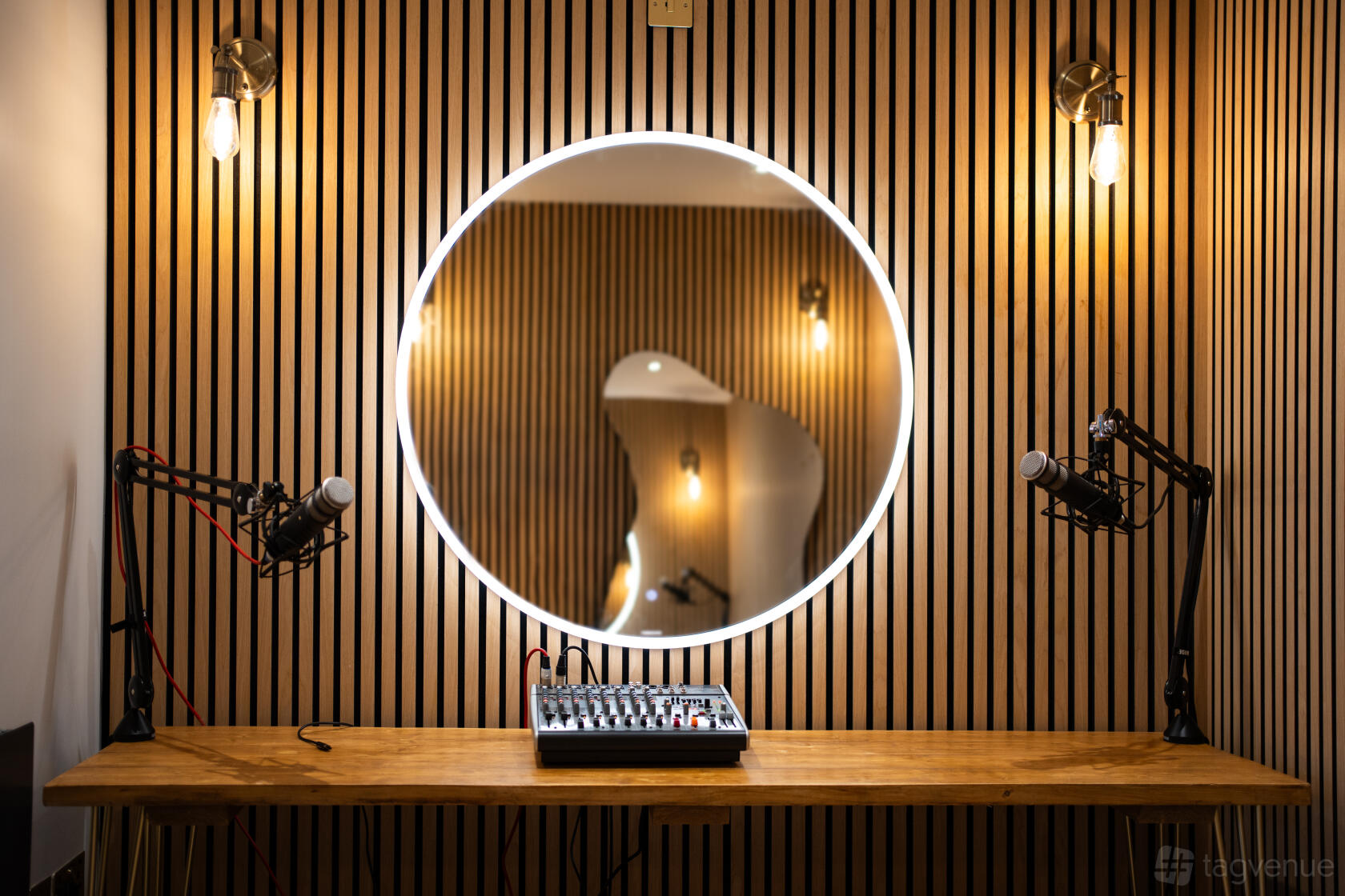 A recording room with a wood slat wall, circular LED mirror, podcast microphones, and audio mixer at Flux Studio.