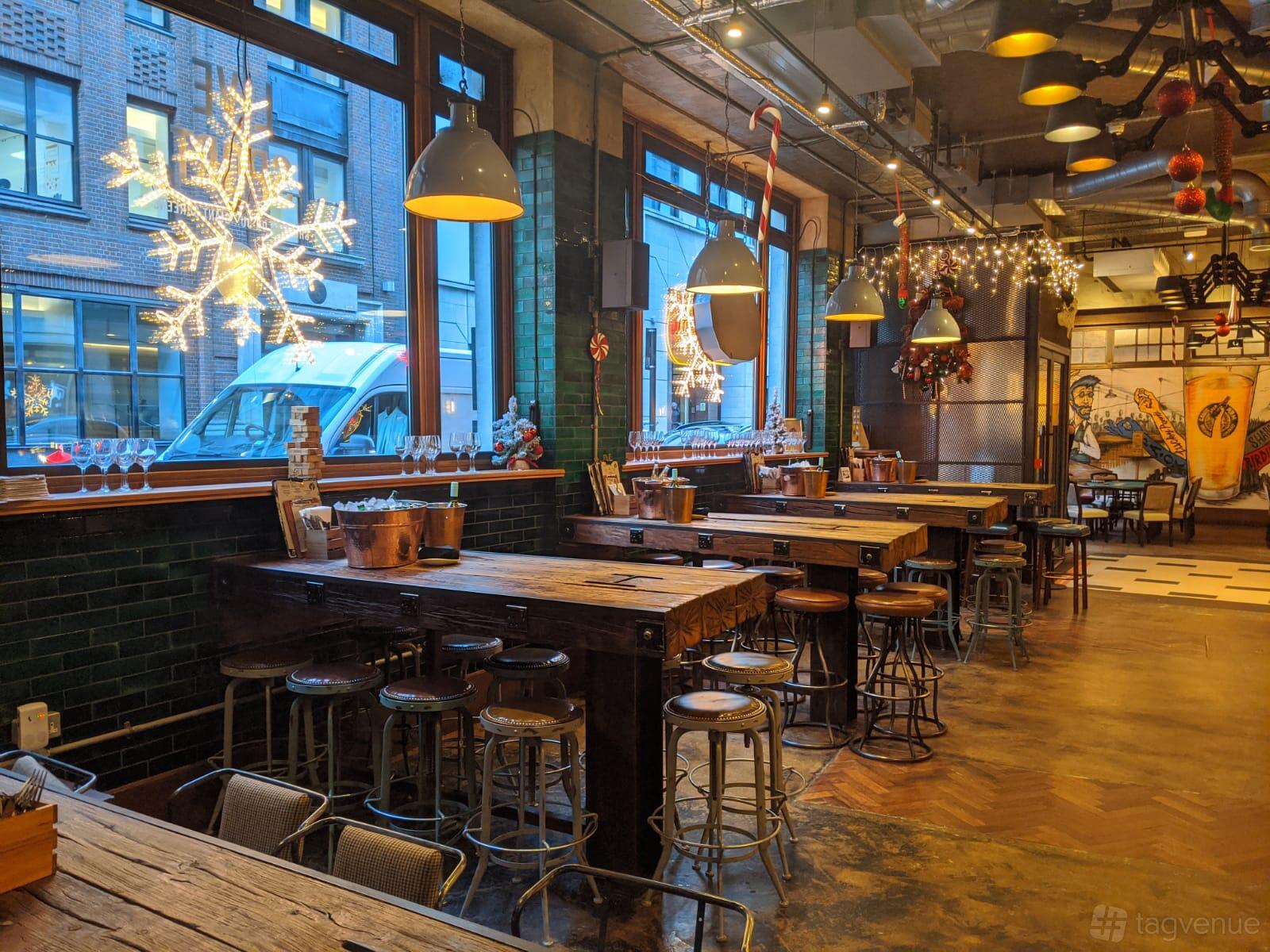 A pub with wooden tables, industrial stools, large windows, and festive string lights at Long Arm Brewery & Tap Room.