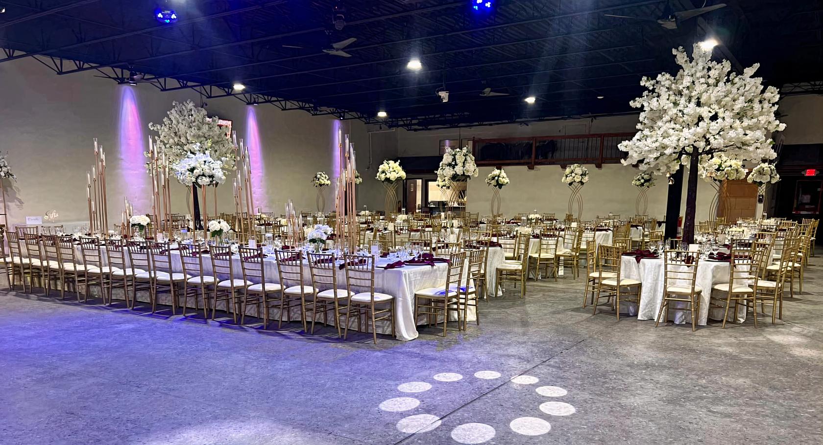 An event venue with long banquet tables, gold chairs, and tall floral centerpieces at Oasis Event Center.