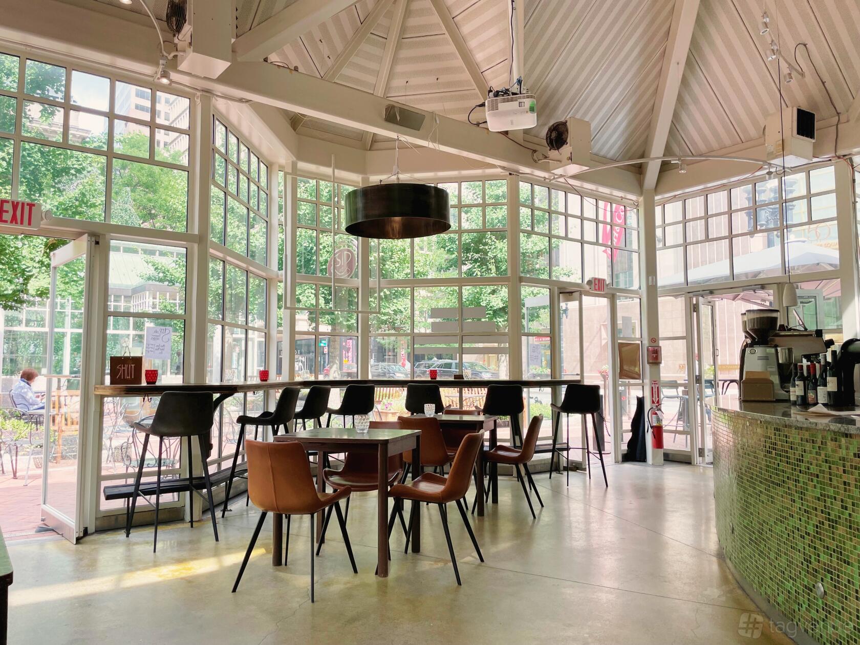 A cafe with floor-to-ceiling windows, natural light, and modern chairs around square tables at Sip Café.