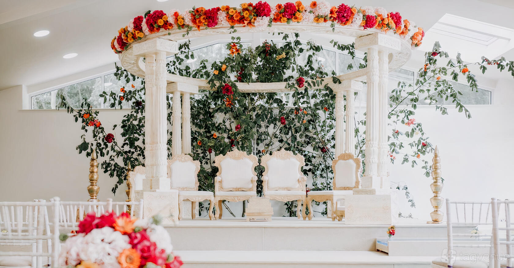 An event venue with an ornate white mandap, floral arrangements, and carved chairs at Ladywood Estate.