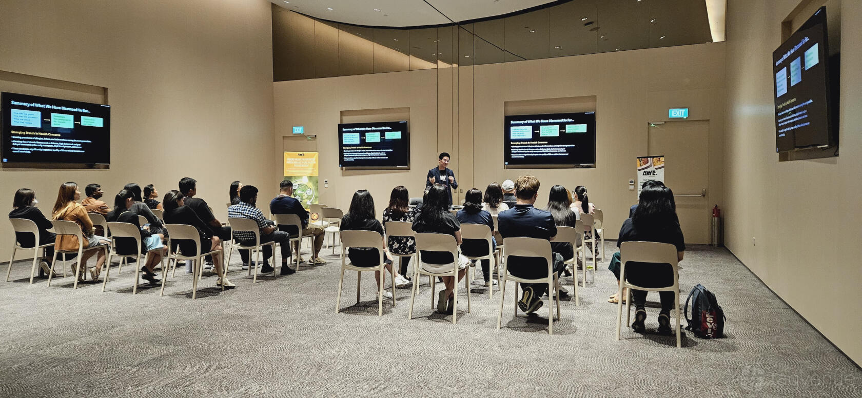A classroom setup with rows of white chairs facing dual wall-mounted screens in Surbana Jurong Campus.