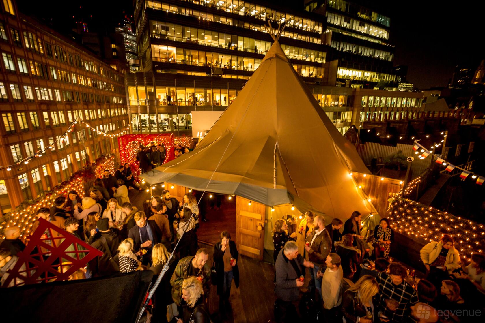 A rooftop nightclub with a large tipi tent, festoon lights, and a crowd of guests at Queen of Hoxton.