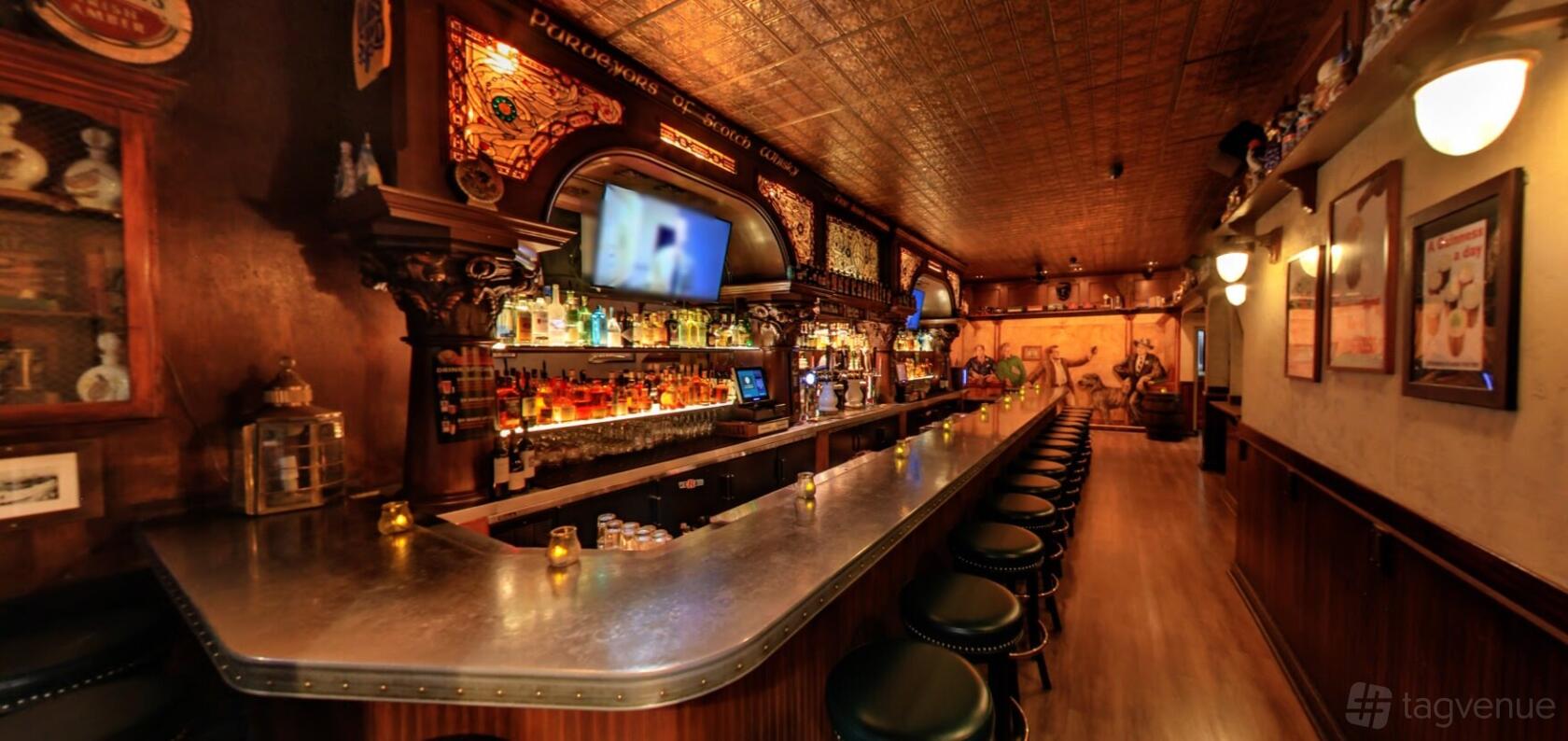 An event space in a pub with a long polished bar, backlit shelves, leather bar stools, and ornate wood accents at Chief Sullivan's.