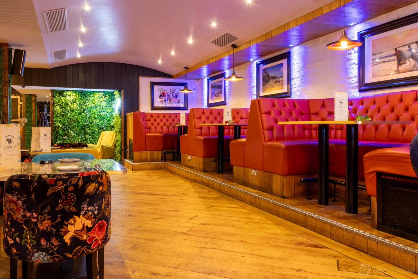 A restaurant with red tufted booth seating, wooden floors, and colorful accent lighting at DeBaga Chapel Allerton.