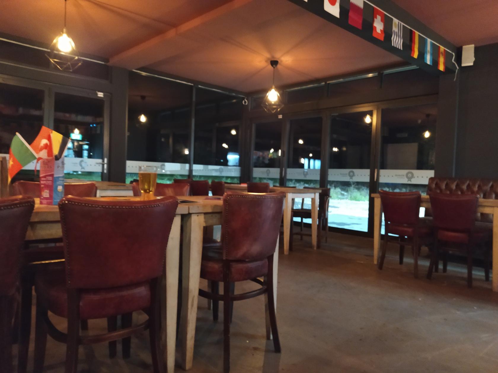 A cafe with wooden tables, brown leather chairs, pendant lighting, and floor-to-ceiling windows at Windmill Leisure Golf & Activity Centre.
