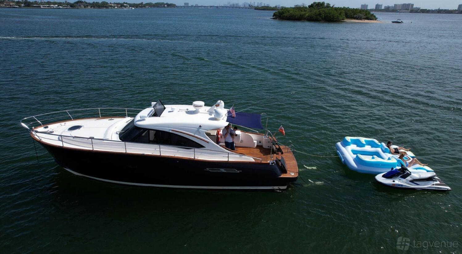 A charter boat with an upper deck canopy and swim platform, anchored near inflatable floats at Luxe Charters.