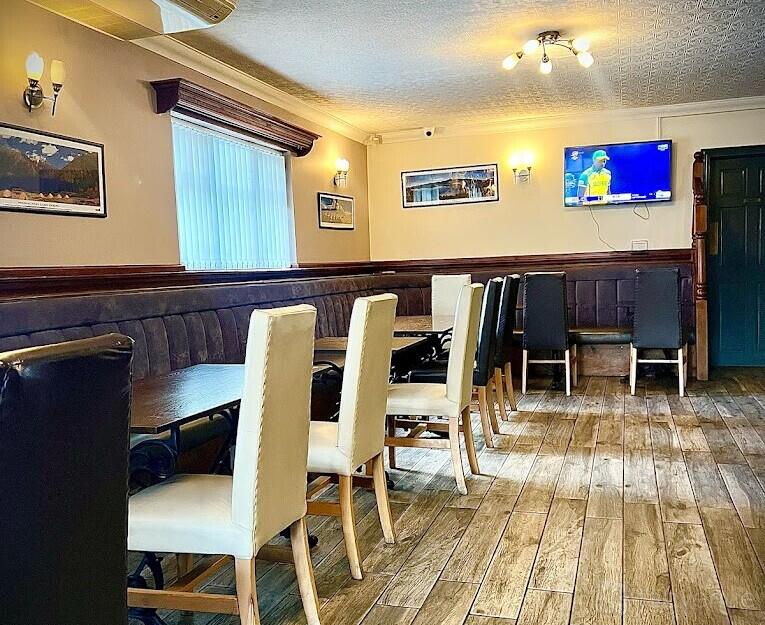 A restaurant with wood floors, long tables with cushioned chairs, wall art, and a mounted TV at Boatmans Food and Grill.