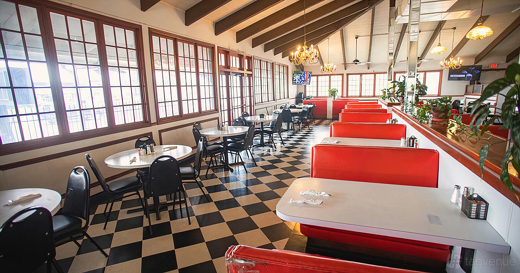 A restaurant with checkered floors, red booths, round tables, and exposed beam ceilings at Victor's Restaurant.