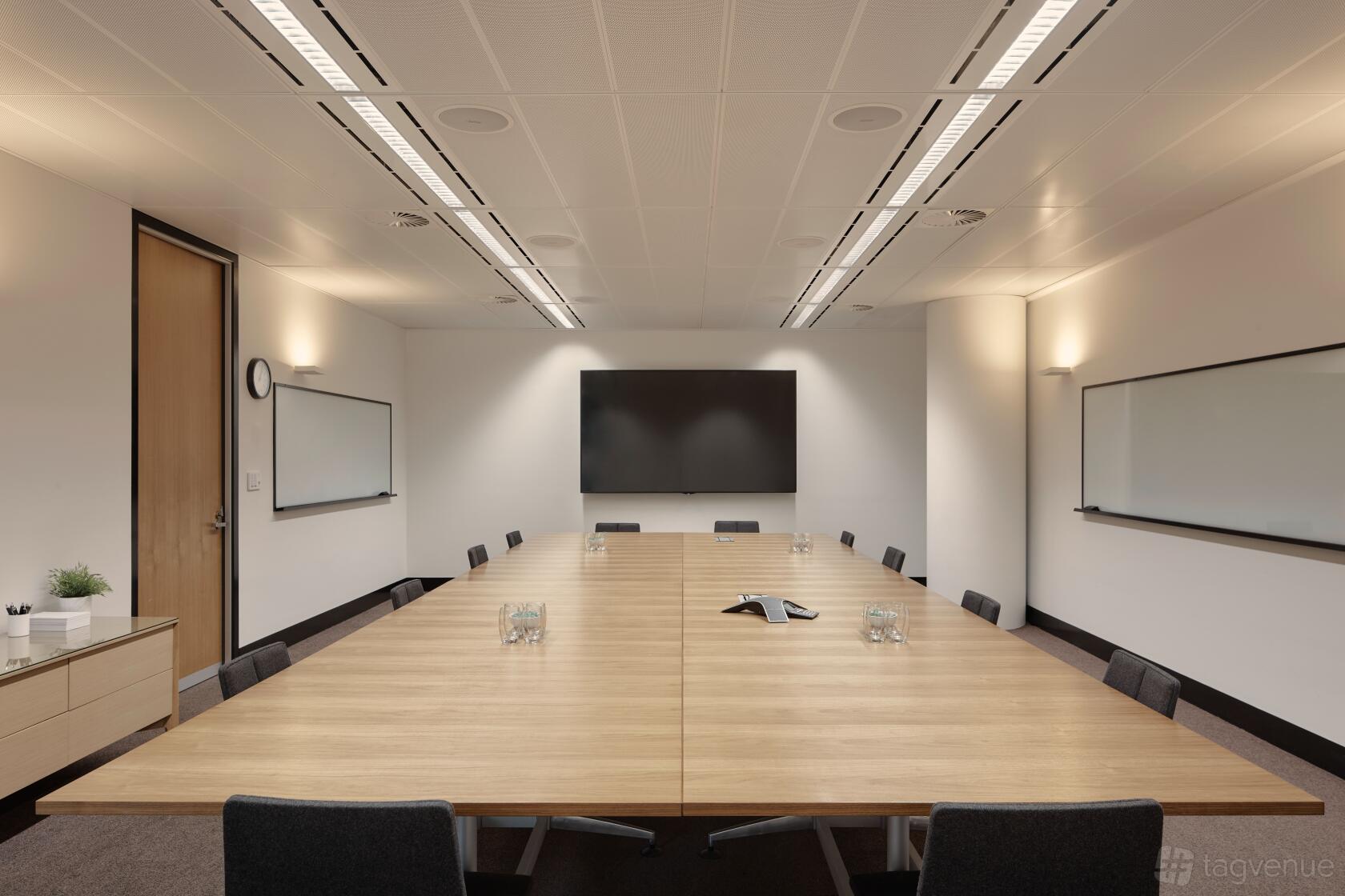 A boardroom with a large wooden conference table, wall-mounted screens, and whiteboards at Flex by ISPT at 4 National Circuit.