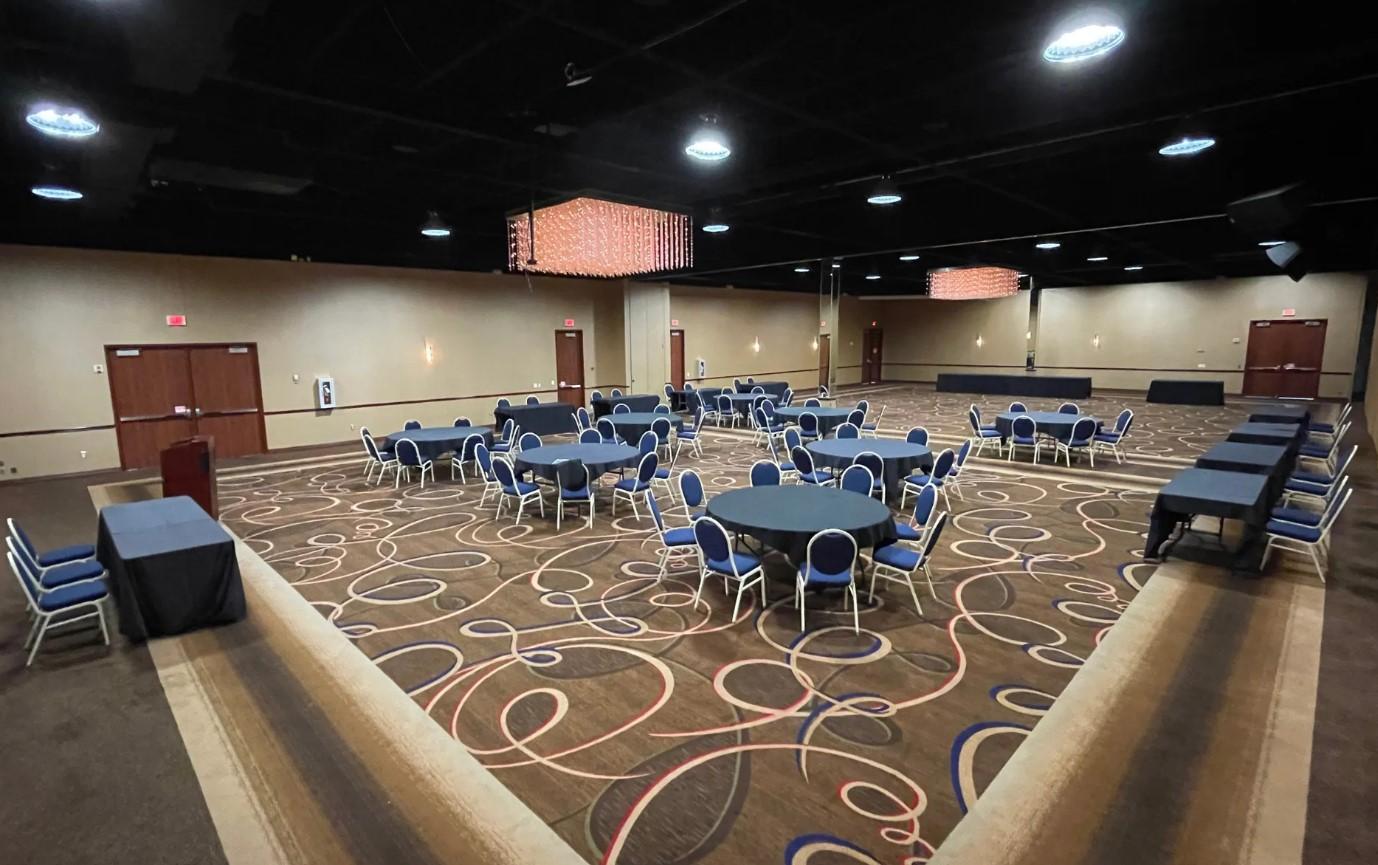 A ballroom with round tables, blue chairs, patterned carpet, and pendant lighting at The Community Collective for Houston.