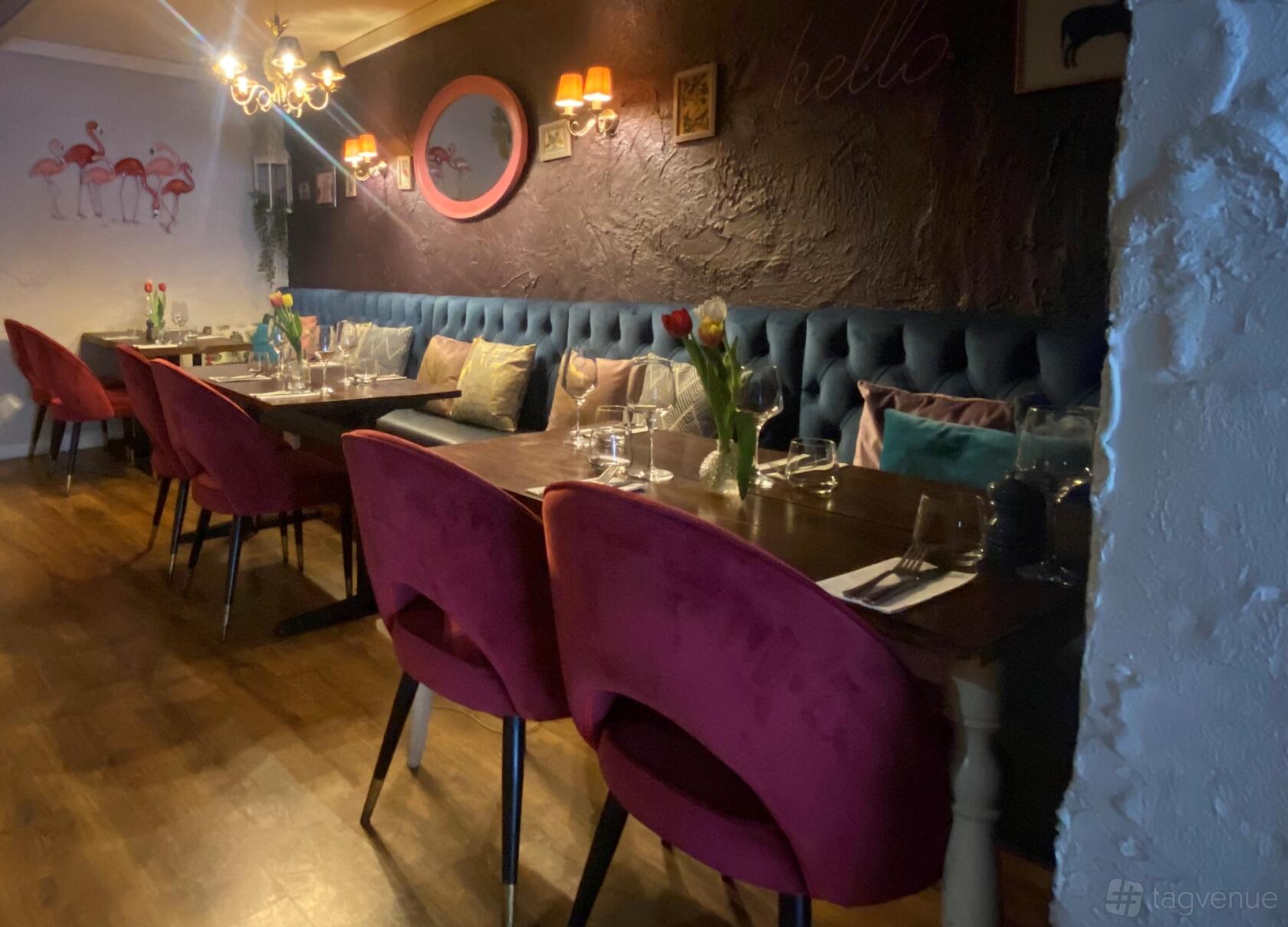 A restaurant dining room with tufted blue banquette seating, pink velvet chairs, and wooden tables at Mosaic Kitchen.