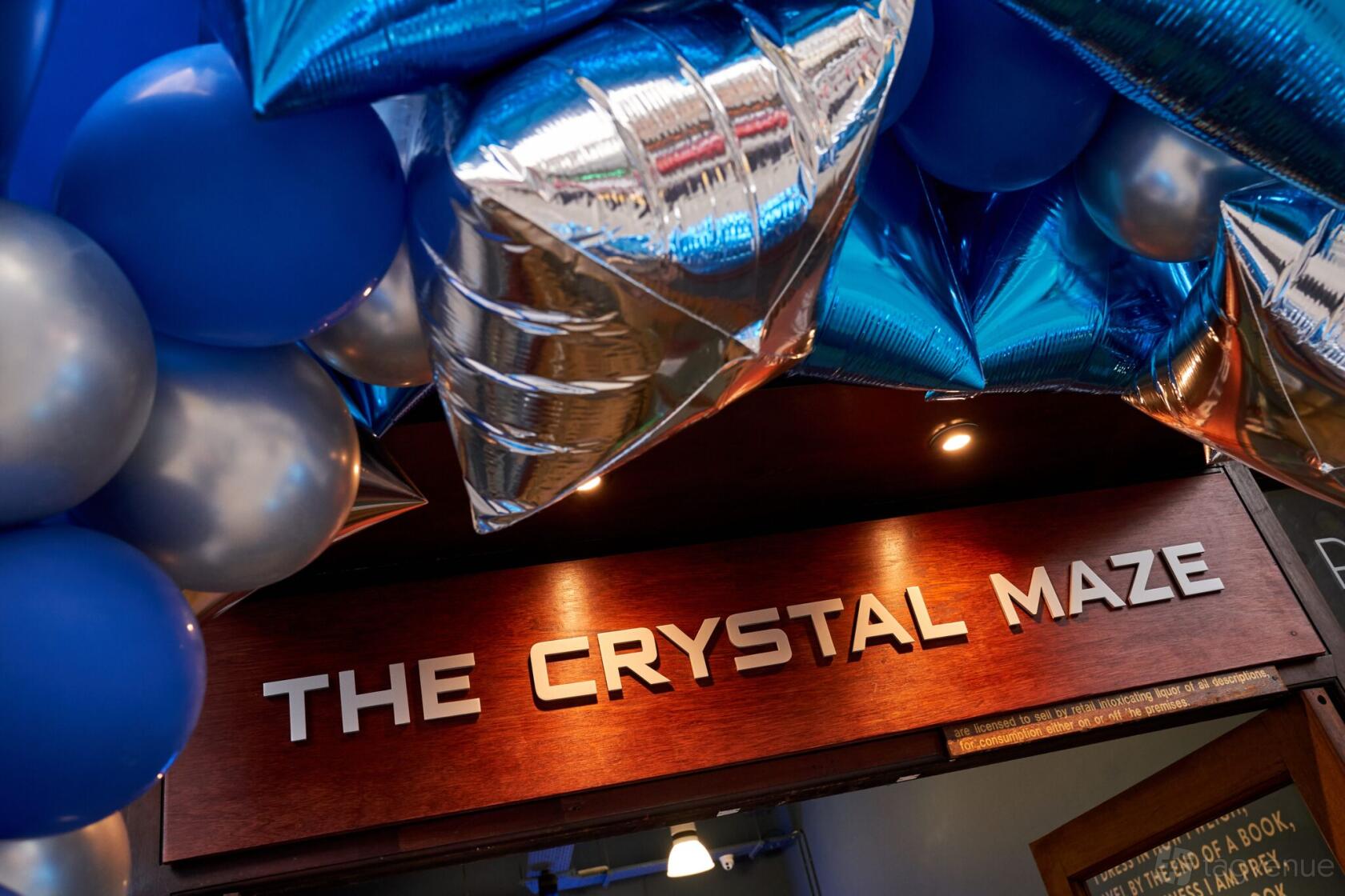 An event space entrance with metallic blue and silver balloons above a sign reading The Crystal Maze LIVE Experience.