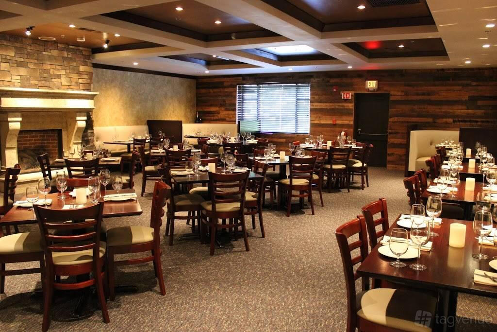 A restaurant with a stone fireplace, wood-paneled walls, and tables set with glassware in Amelia's Tuscan Room.