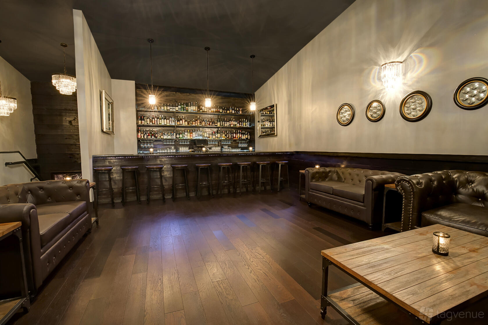 An event space in a bar with leather sofas, wood flooring, and a backlit bar display at The Eleanor.
