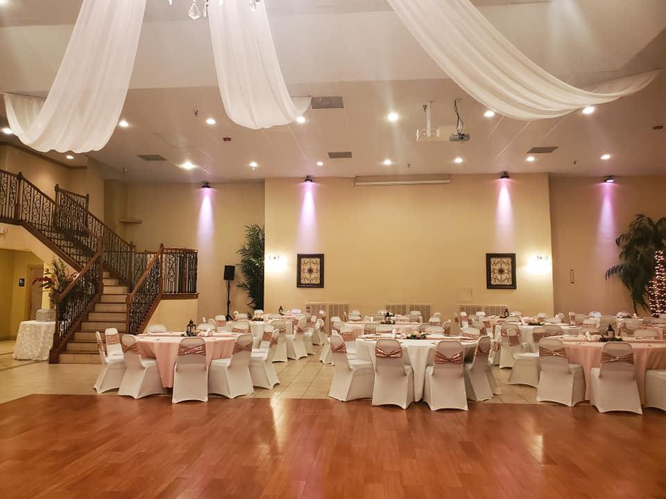 An event venue with draped white fabric on the ceiling, round tables with pink linens, and a staircase at Dolce Villa Events LLC.