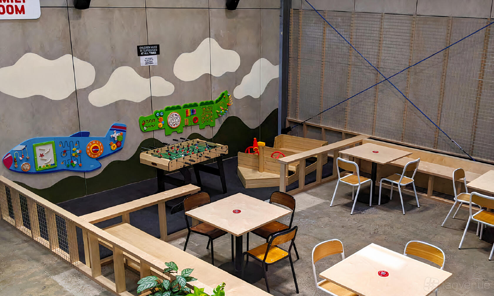 An event space in a brewery with a fenced play area, wall games, foosball table, and simple wooden tables at Co-Conspirators Brewpub.