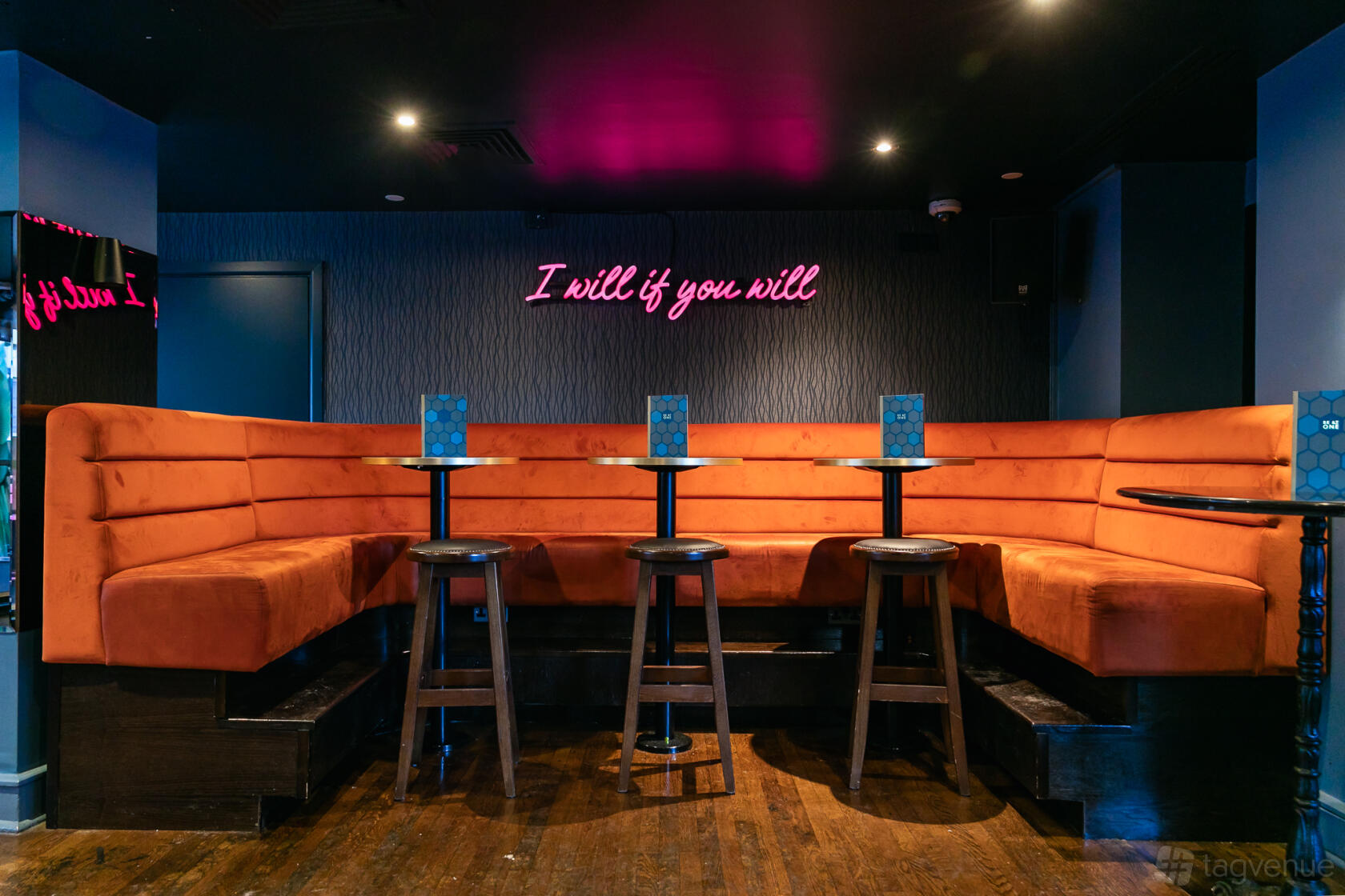 A function room with orange velvet banquette seating, high tables, and a neon wall sign at Be At One Liverpool Street.