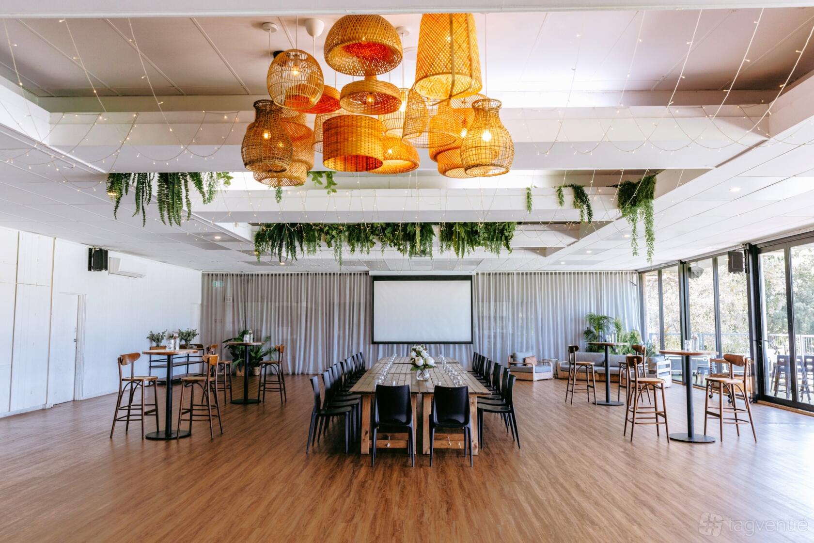 An event space in a bar with wooden floors, hanging wicker lamps, greenery, and floor-to-ceiling windows at The Field Bar.