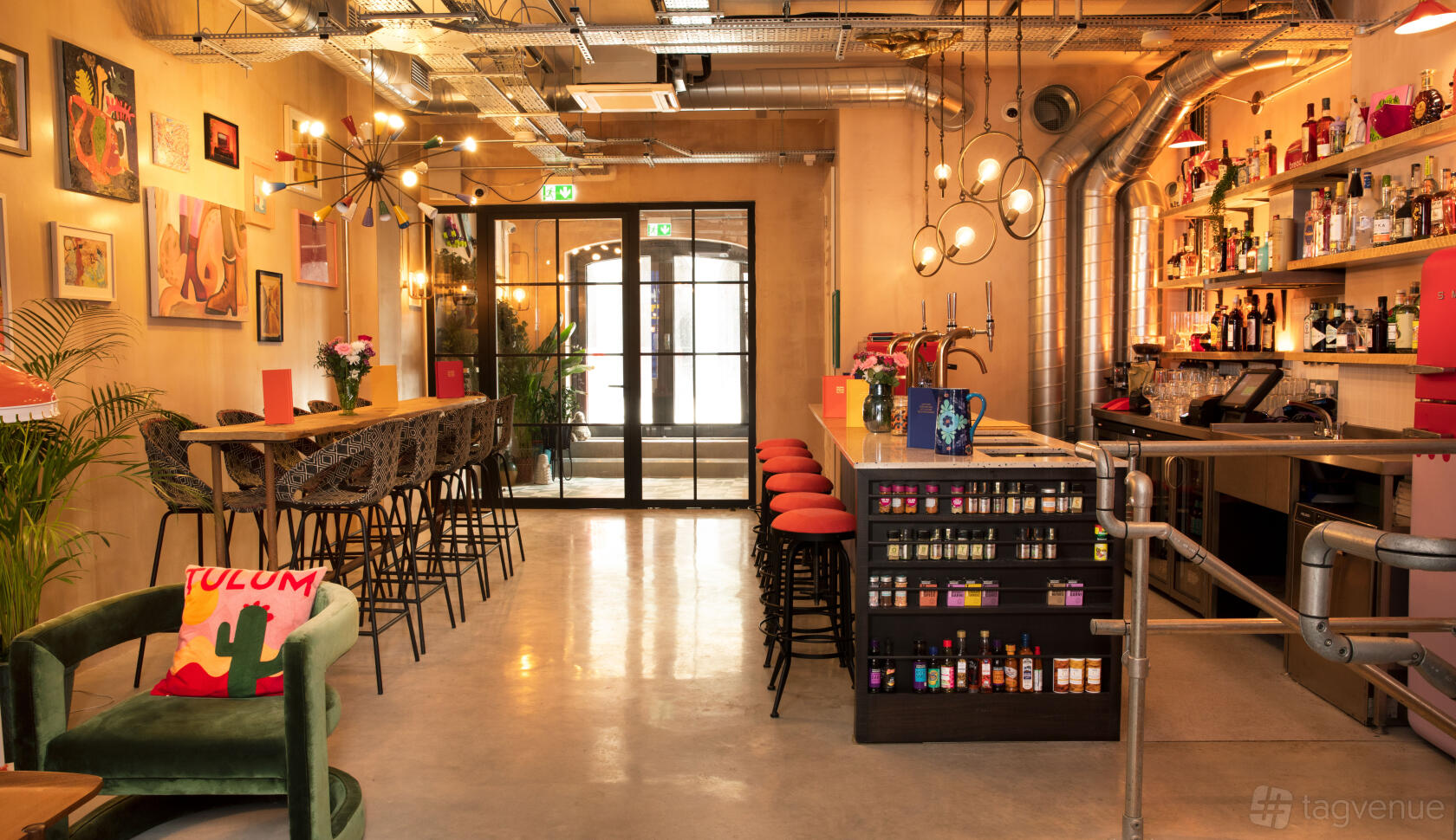An event space in a cocktail bar with high-top tables, bar stools, eclectic decor, and wall art at The Little Scarlet Door.