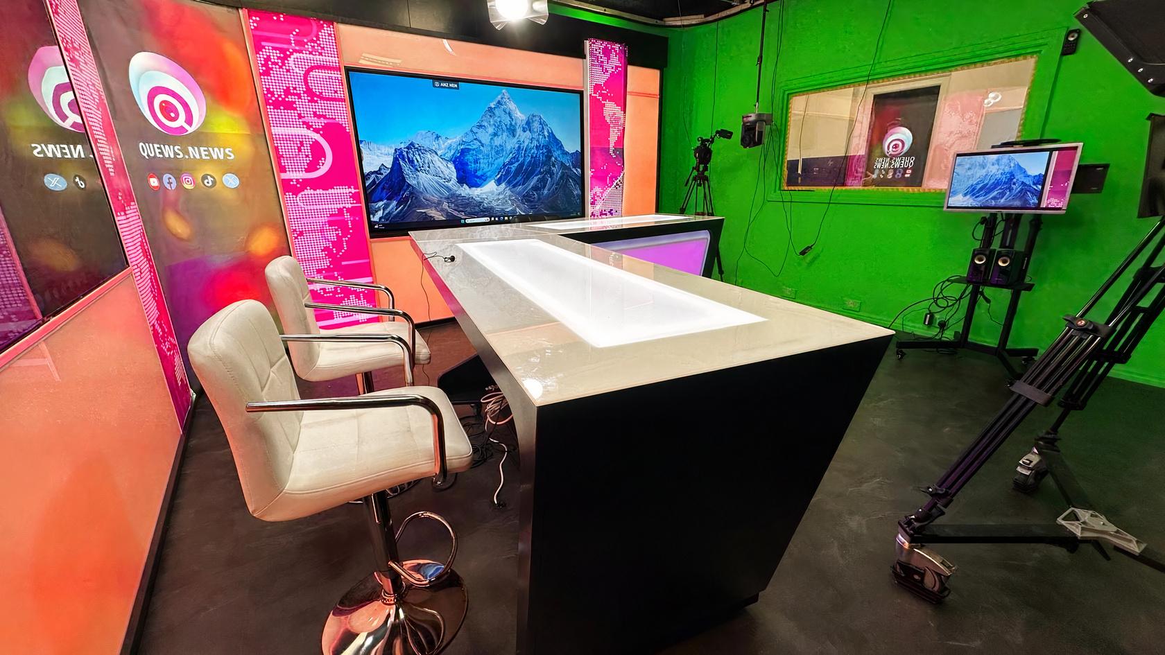 A podcast studio with a white countertop, high chairs, LED screens, and broadcast lighting at Quews Digital Media.