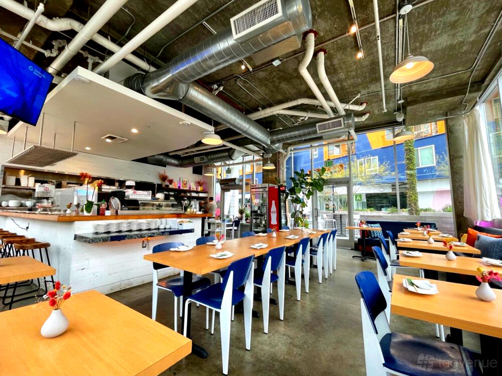 An event space in a restaurant with wooden tables, blue chairs, and exposed ductwork at Kombu Sushi Arts District.