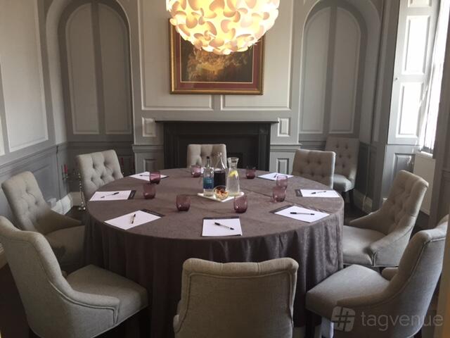 A hotel meeting room with a round table, notepads, glass water bottles, and upholstered chairs at The Highworth Hotel.