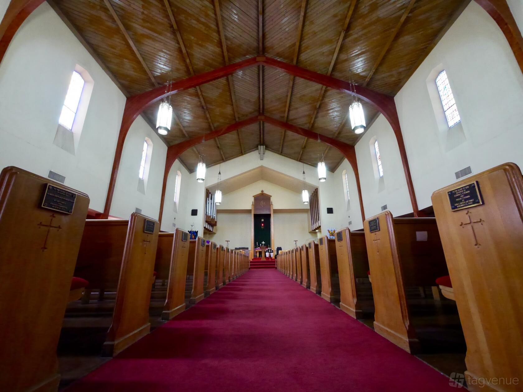 A church with wooden pews, high vaulted ceiling, hanging pendant lights, and red carpet aisle at Church 01.