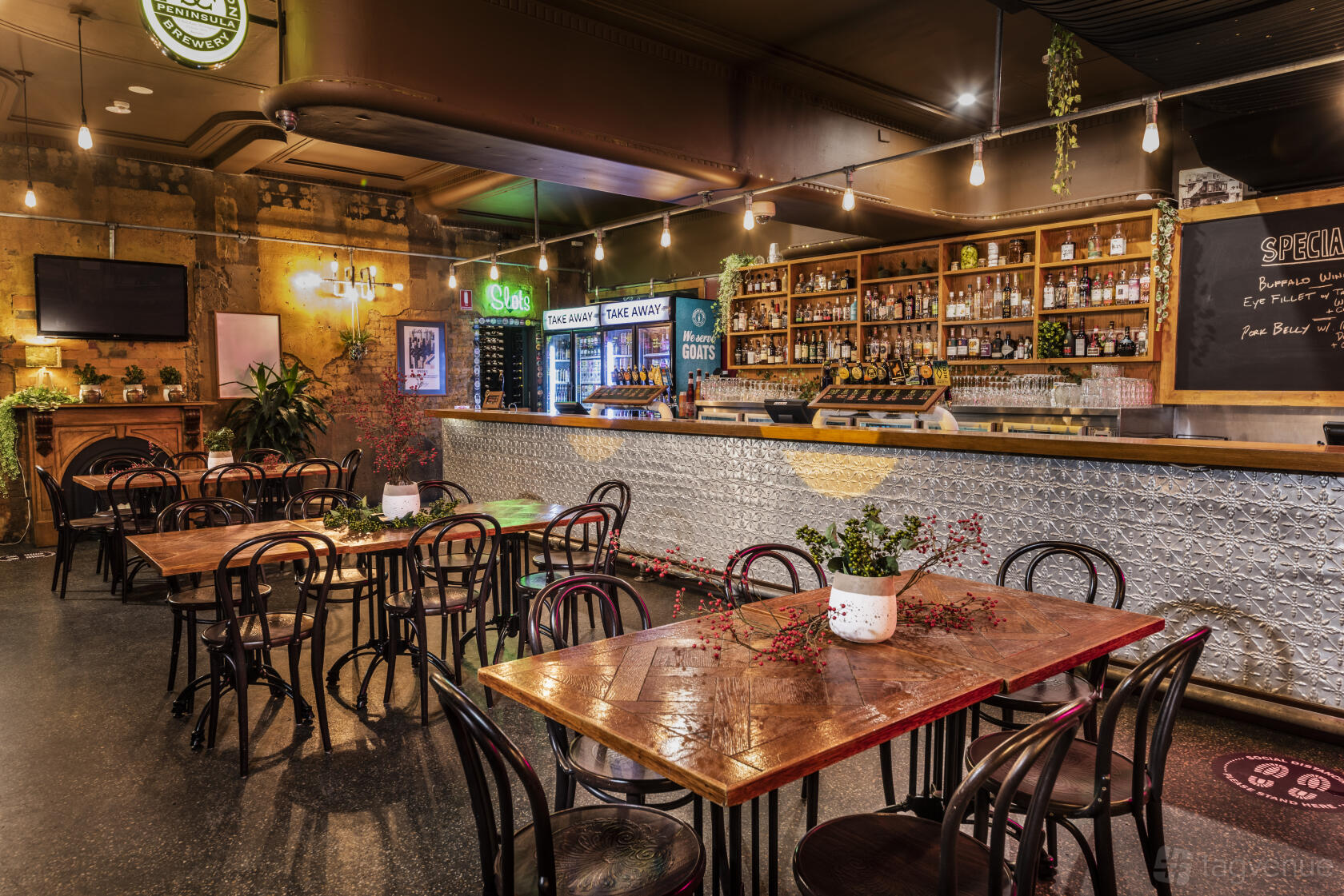 A bar with wooden tables, black bentwood chairs, a metal-clad bar counter, and shelves of spirits at Embassy Hotel.