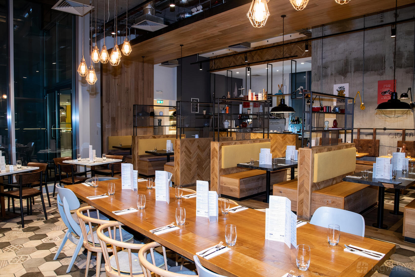 A restaurant with wooden tables set with menus and glassware, pendant lighting, and booth seating at Takaa tak Hayes.