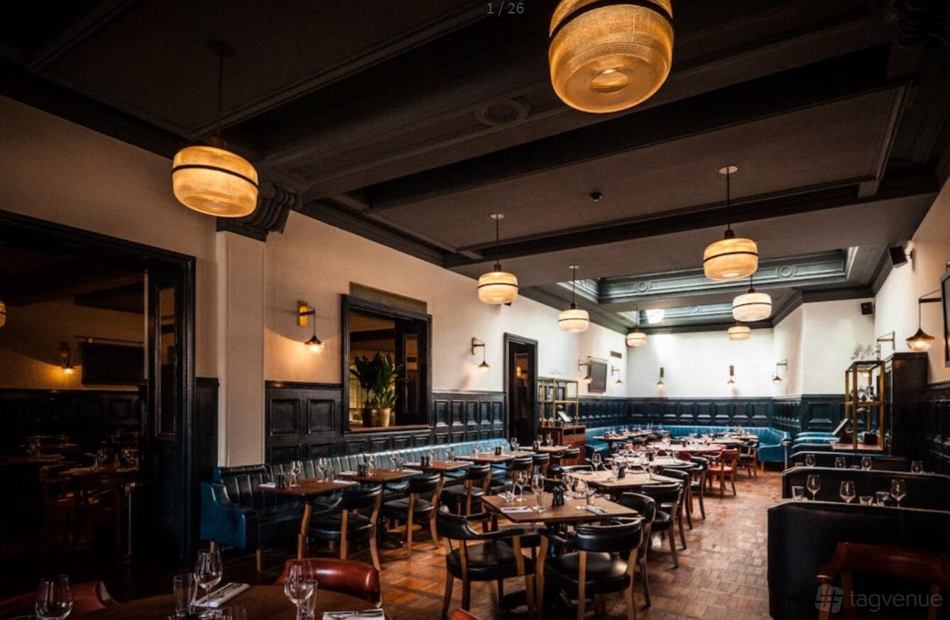 A restaurant dining room with dark wood furniture, leather banquettes, and pendant lighting at Hawksmoor Manchester.