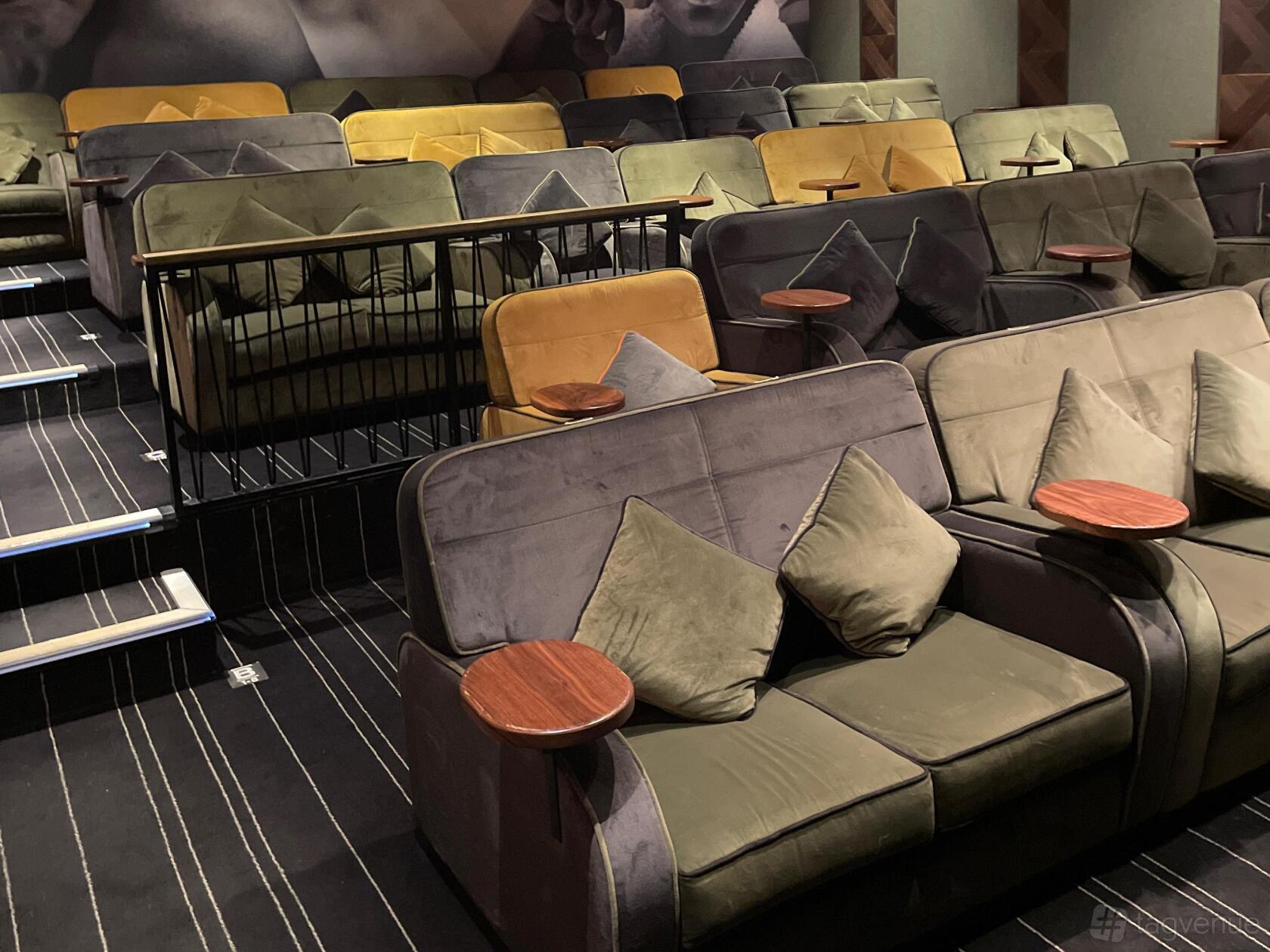 An auditorium with plush sofa seating, individual side tables, and striped carpeting at Everyman Gerrards Cross.