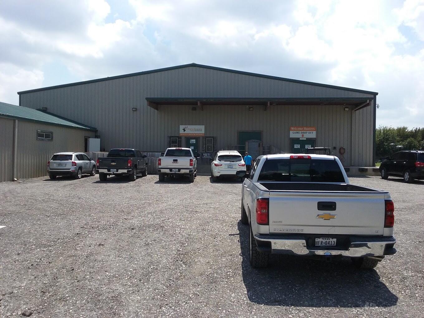 A metal event barn with a gravel parking lot and several parked vehicles at Cinnamon Creek Ranch.