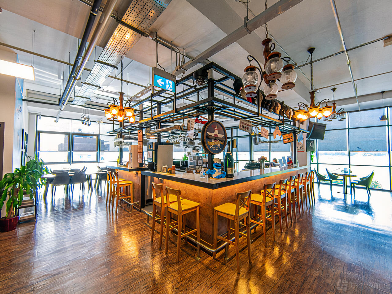 A cafe with a central island bar, hanging lanterns, aviation decor, and yellow stools at WingsOverAsia.