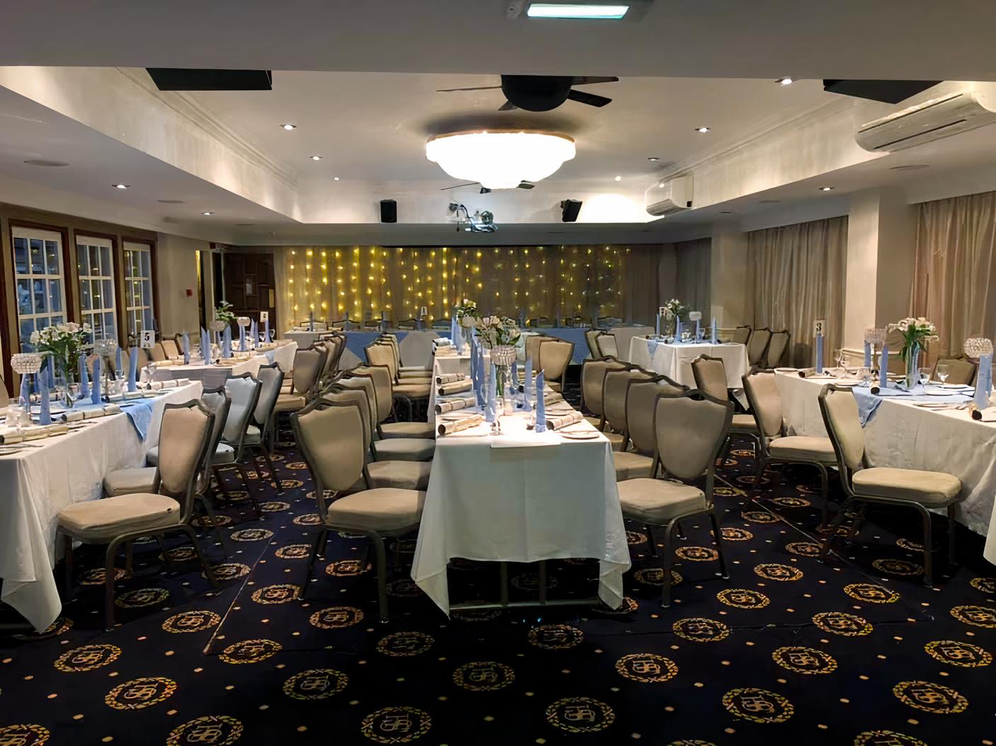 An event space in a hotel with long banquet tables, upholstered chairs, and a backdrop of string lights at Santo's Higham Farm Hotel.