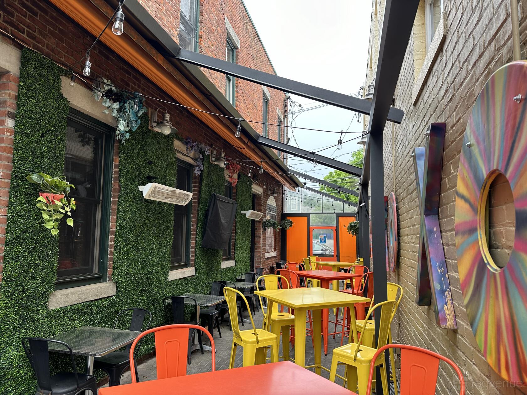 An outdoor bar patio with yellow and red chairs, high tables, string lights, and faux greenery at The Biltmore Bar & Grille.