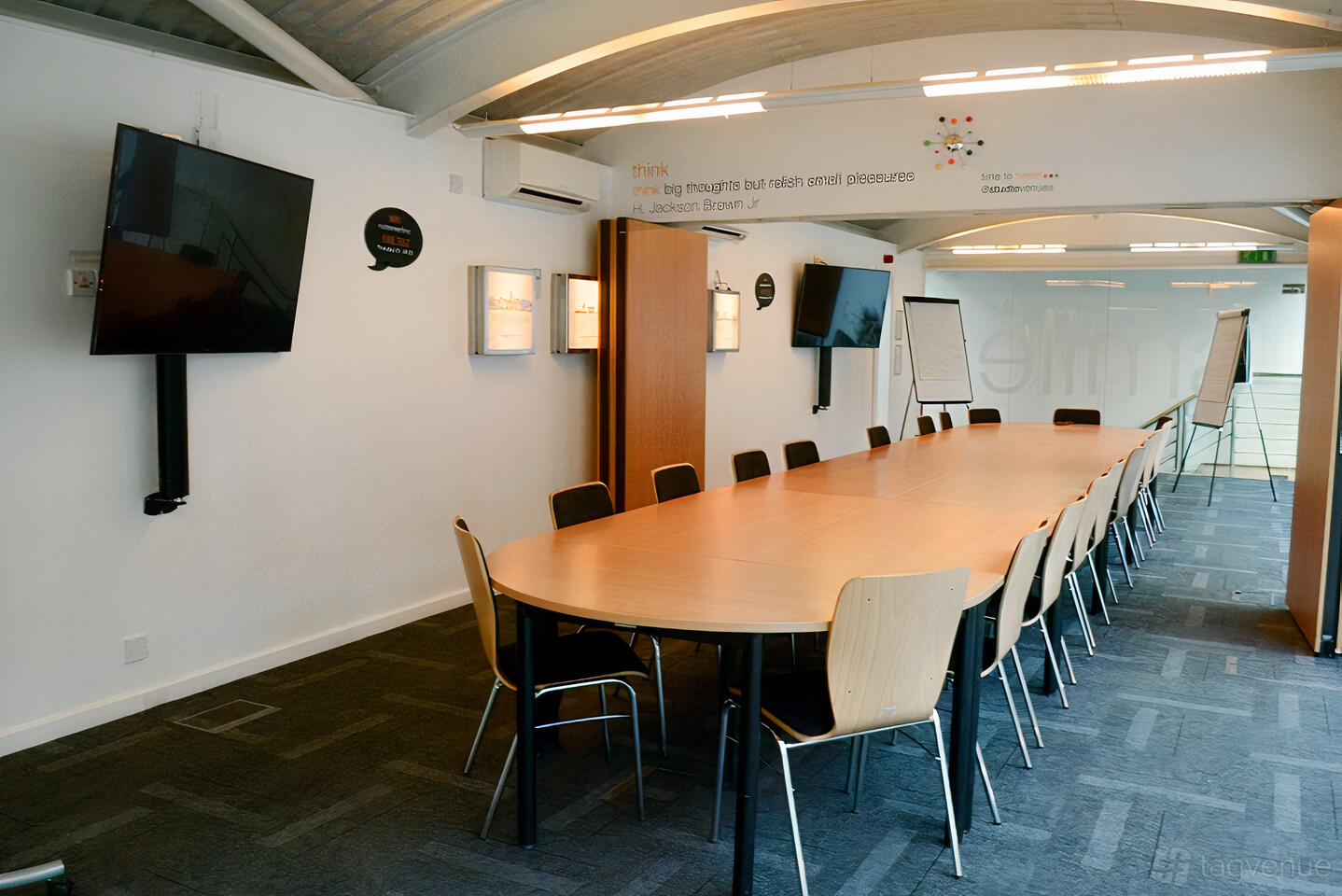 A meeting room with a long oval conference table, wall-mounted TV screens, and flip charts at The Studio Birmingham.