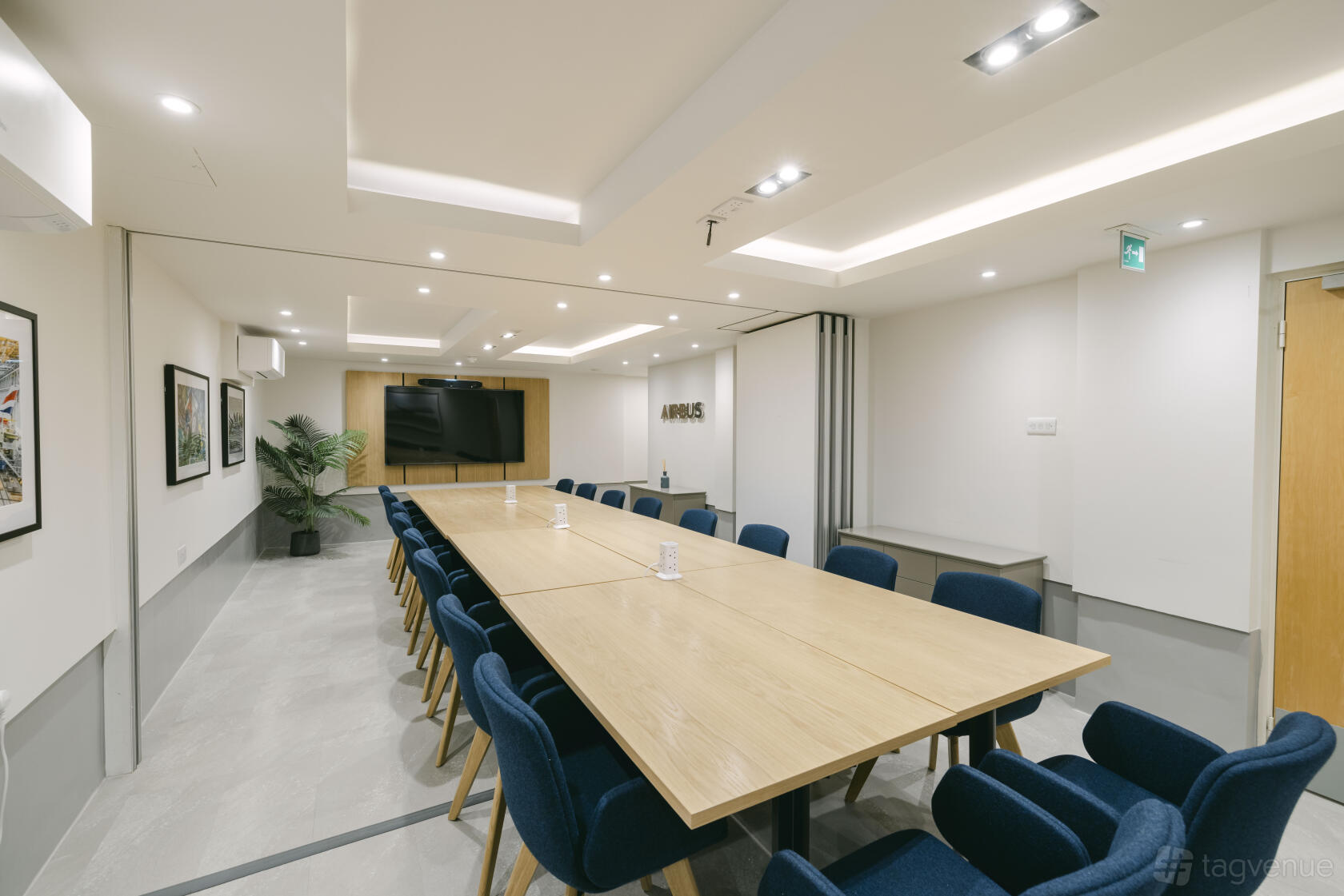 A meeting room with a long wooden table, blue upholstered chairs, built-in screen, and wall art at No. 4 Hamilton Place.
