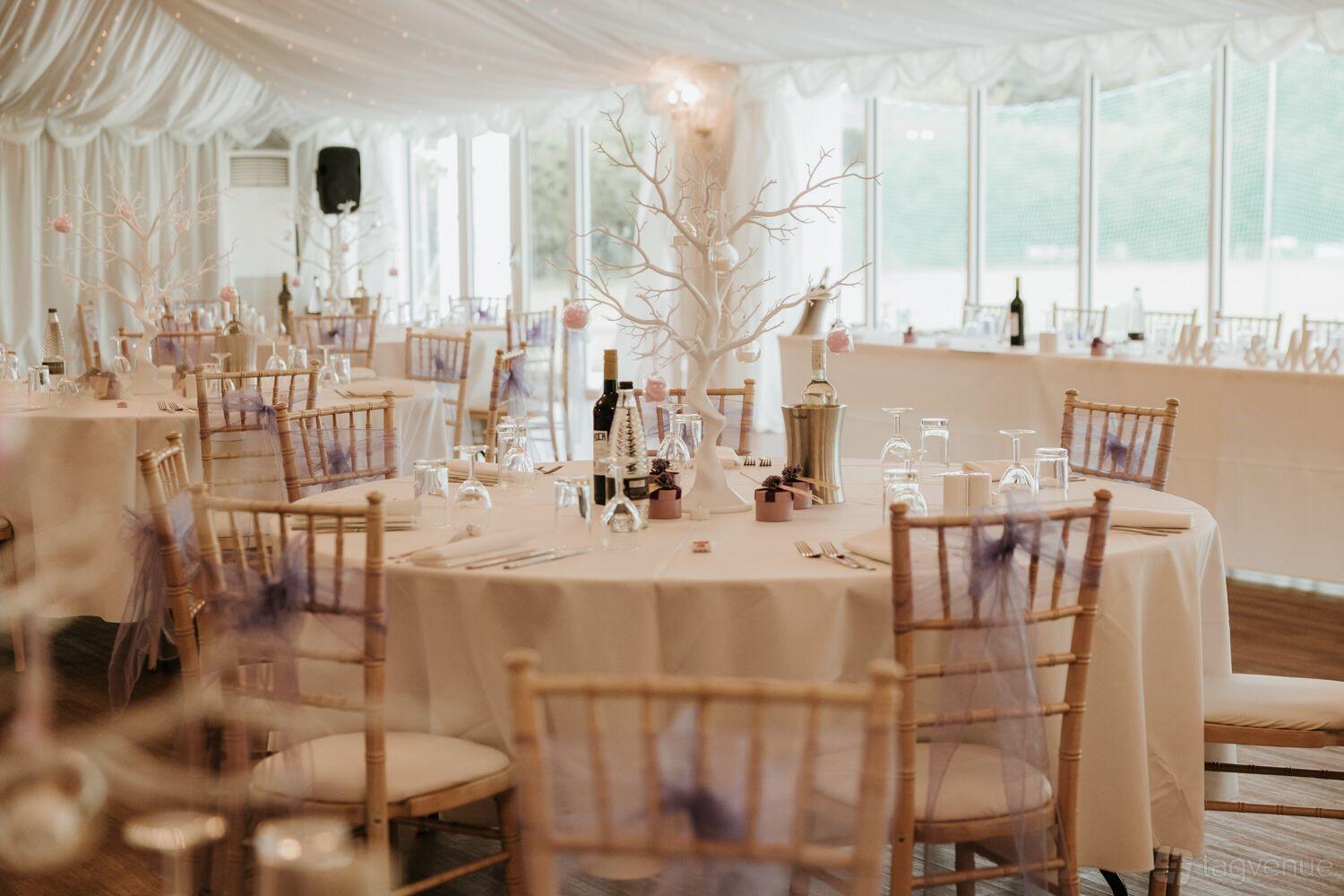 A hall with round tables set with white linens, chiavari chairs, and sheer draping at London Shenley Club.