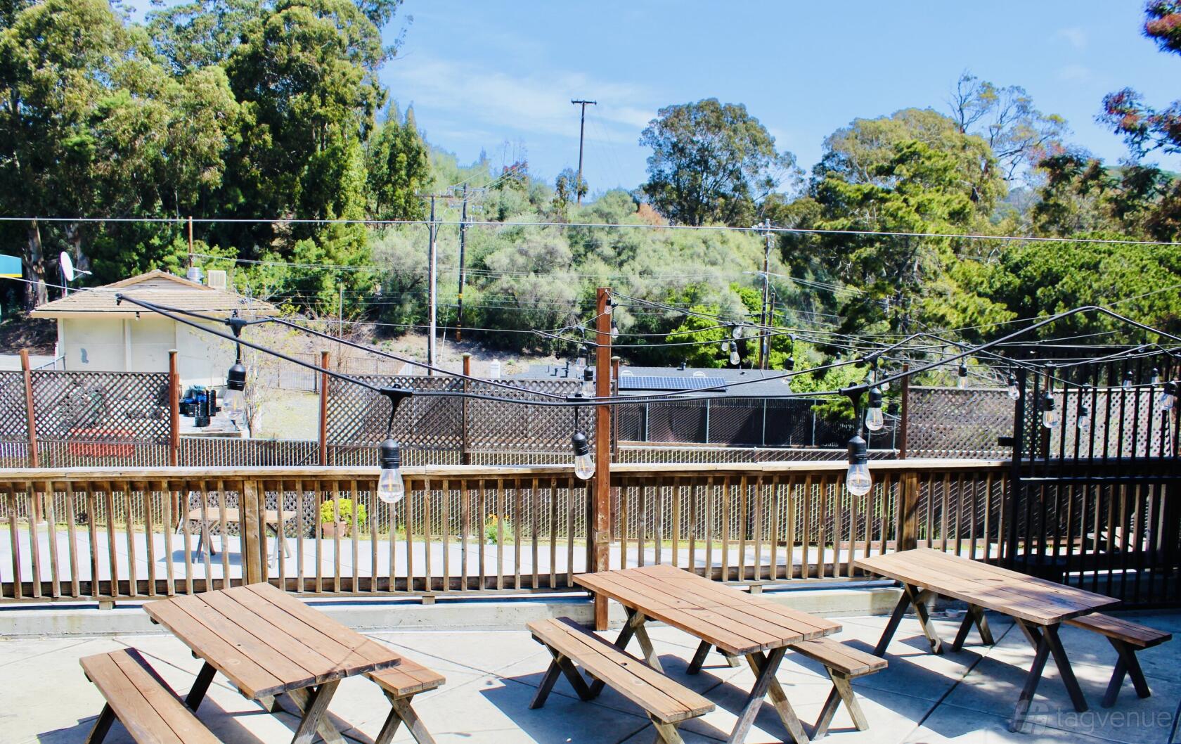 An outdoor dining area with wooden picnic tables, string lights, and a wood railing at Roderick's BBQ.