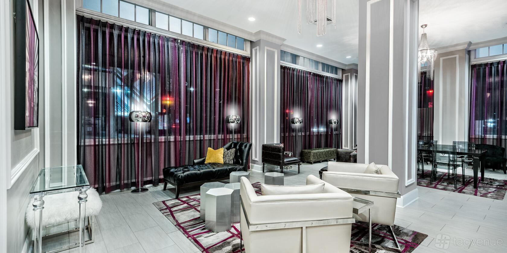 A hotel library with floor-to-ceiling windows, sheer drapes, armchairs, and modern lamps at Hotel Indigo Dallas Downtown.