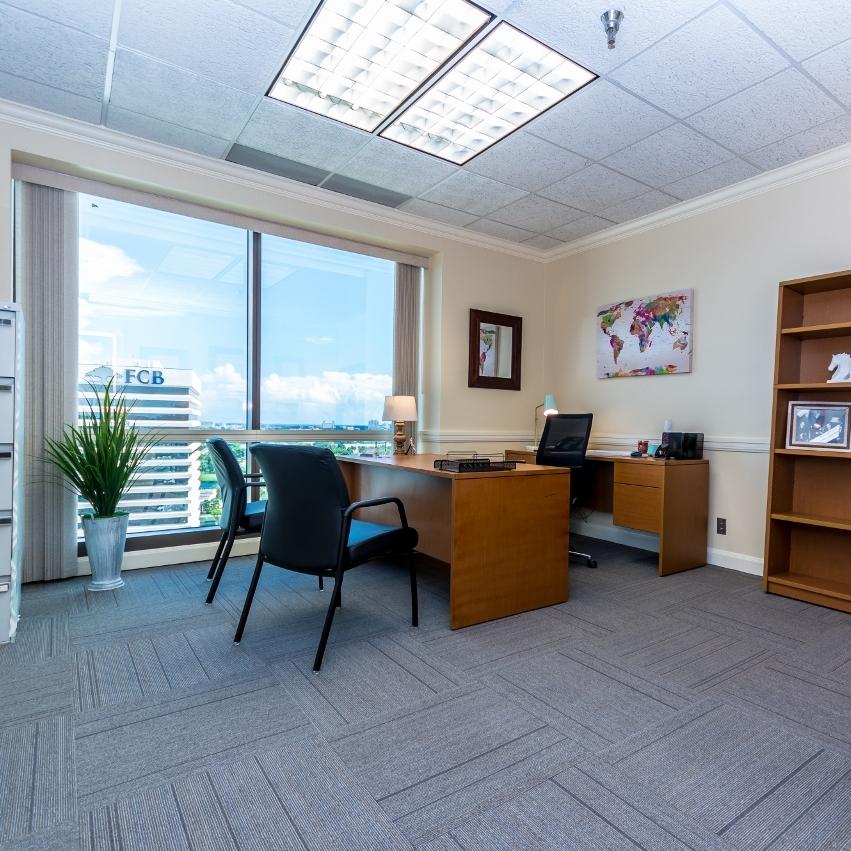 A meeting room with a large window, wooden desk, map wall art, and an office chair at ZEN Offices West Palm Beach.
