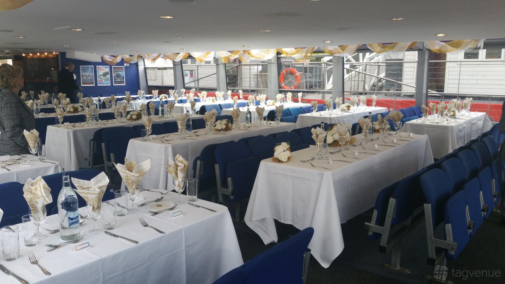 An event space on a boat with rows of tables set with folded napkins and blue chairs at City Cruises Ltd.
