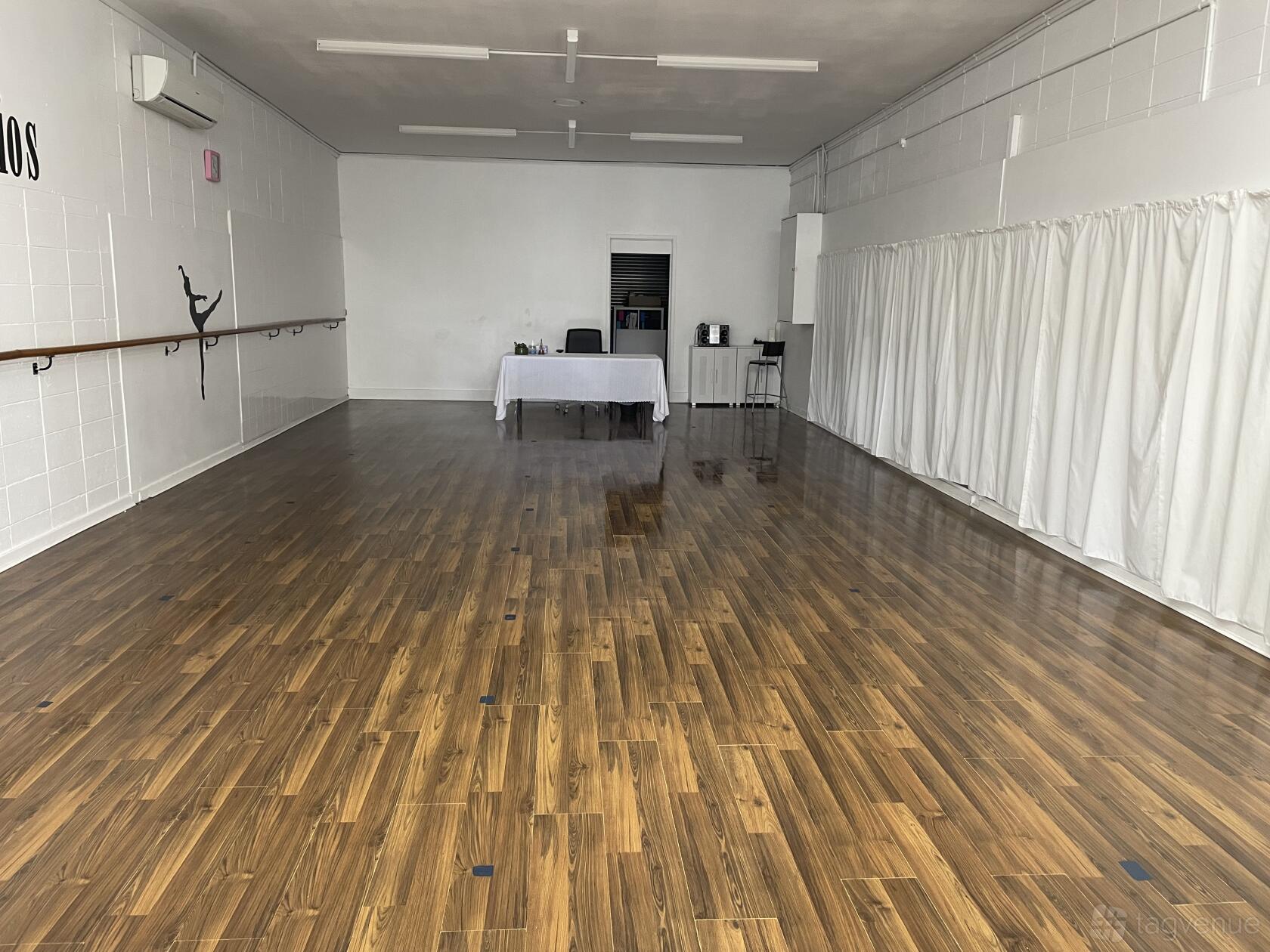 A dance studio with wood flooring, mirrored walls, ballet barres, and floor-to-ceiling curtains at Vibe Dance Studios.