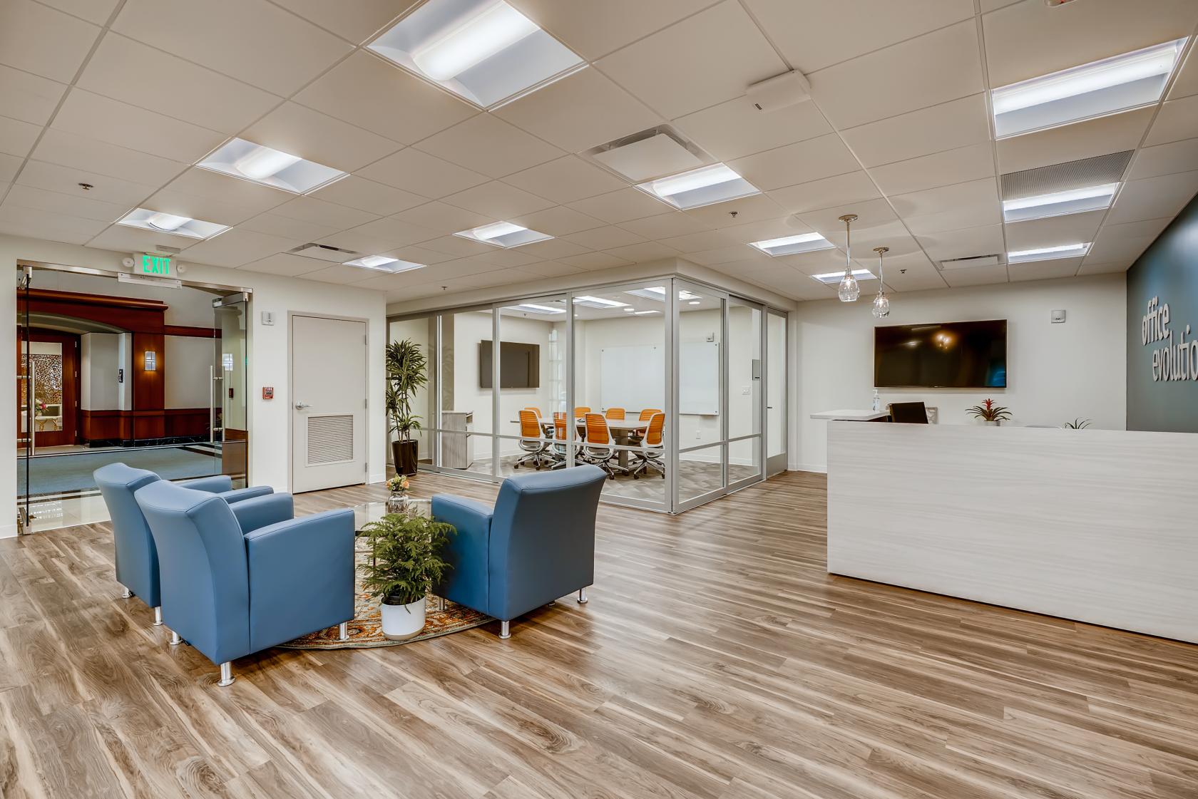 A meeting room with glass walls, a conference table, and orange chairs at Office Evolution Johns Creek - Duluth.