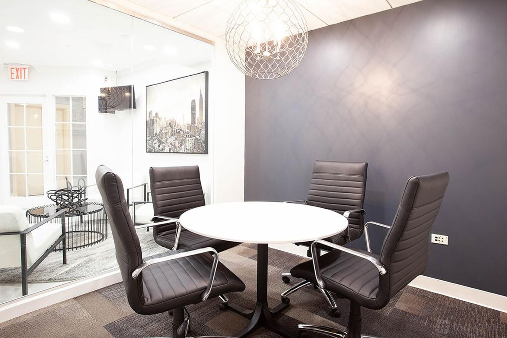 A coworking space with a round white table, four black leather chairs, and a glass wall at Premier Workspaces - Midtown Manhattan.