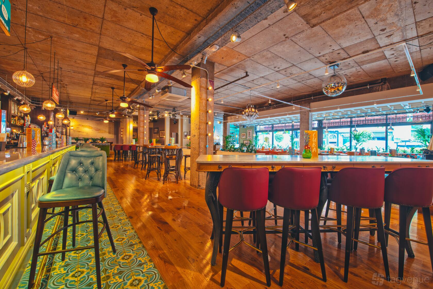 A restaurant with wooden floors, exposed concrete ceiling, a tiled bar, and velvet chairs at Revolucion de Cuba Newcastle.
