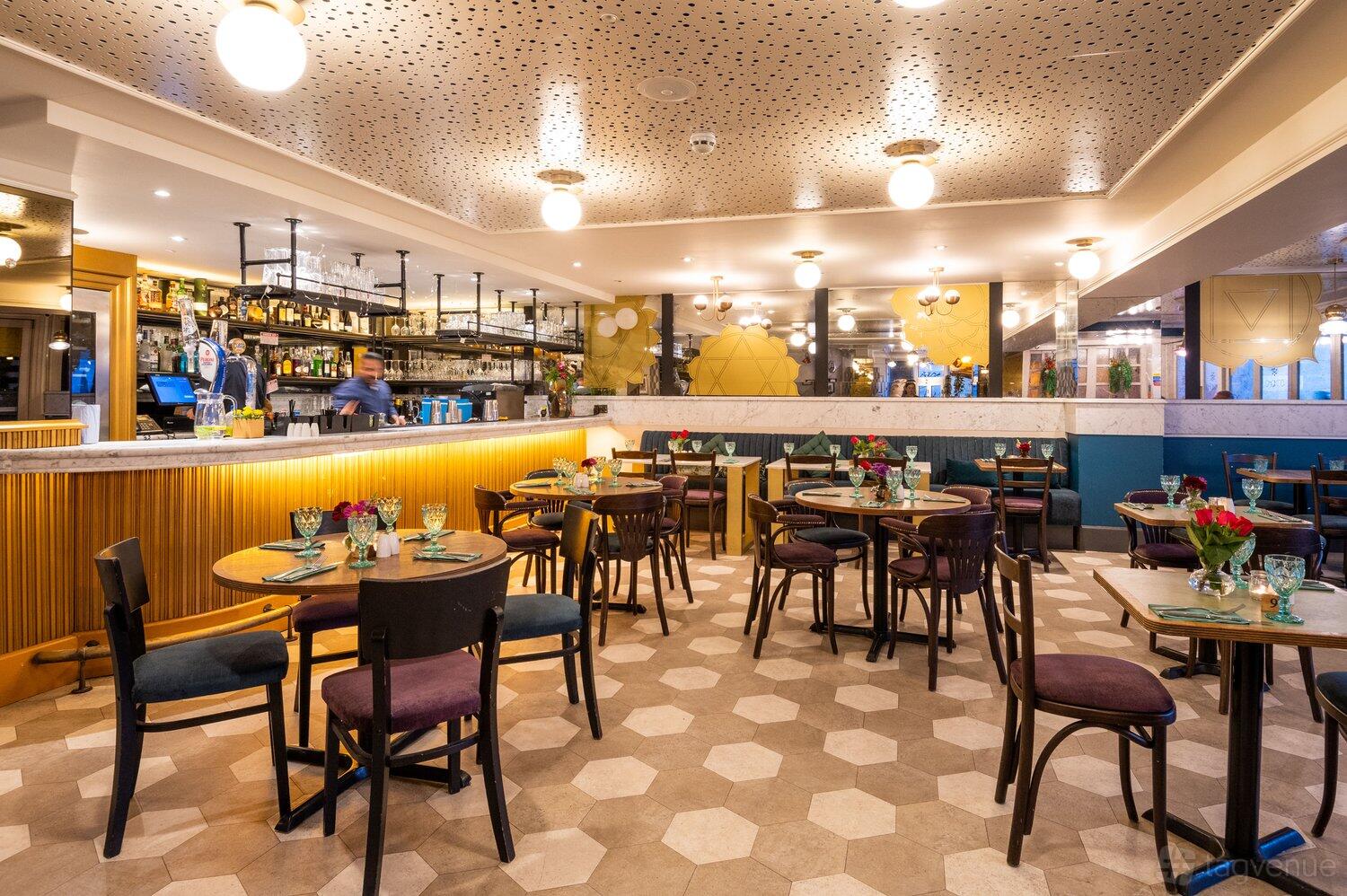 A restaurant with hexagonal tile flooring, round tables set with glassware, and a marble bar at Chakra Kingston Upon Thames.