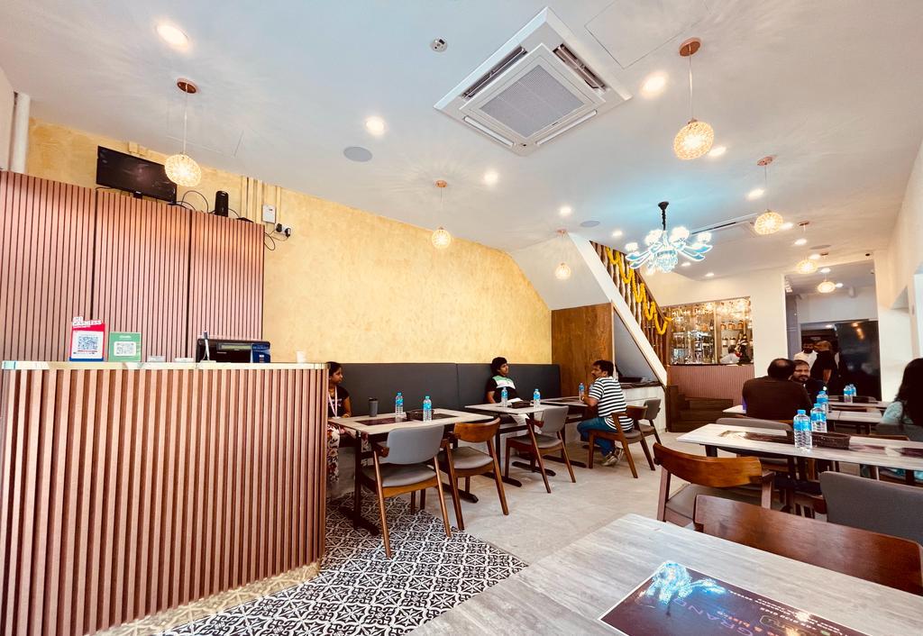 A restaurant with wooden tables, pendant lighting, and a patterned tile floor at SARIGAMA Indian Restaurant.